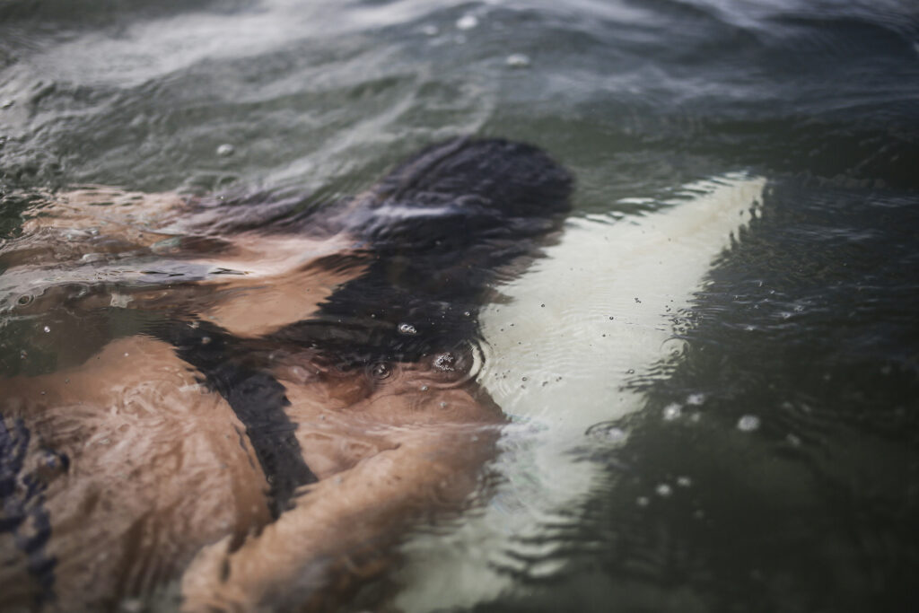 Une femme est visible nageant sous l'eau, allongée sur sa planche de surf. Cette photographie est issue du long reportage réalisé en immersion par Gabriela Tellez (Light Motiv) sur les communautés des femmes surfeuses de l'Océan Pacifique à Nosara au Costa Rica.