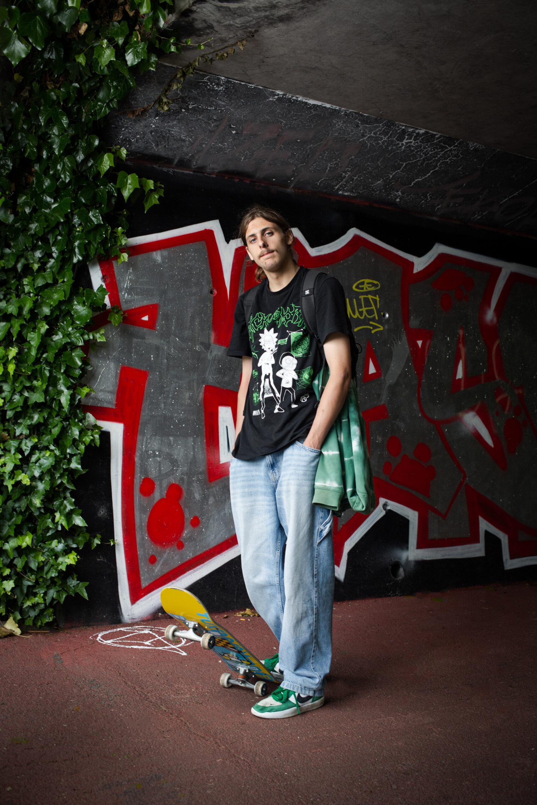 Portrait d'un adolescent posant debout devant un mur recouvert d'un graffiti, avec un skateboard (planche à roulettes) qu'il soulève d'un pied, issu du reportage photographie de Richard Baron (membre de Light Motiv) sur la mobilité urbaine des jeunes à Lille pour le magazine Phosphore, numéro 34, septembre 2024