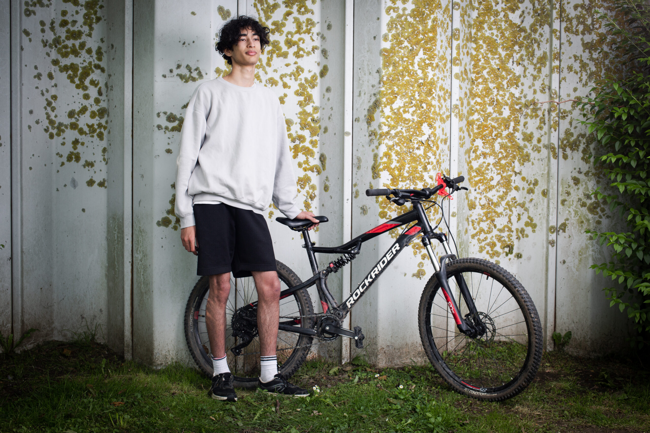 Portrait d'un adolescent posant debout à côté d'un vélo, sur l'herbe, issu du reportage photographie de Richard Baron (membre de Light Motiv) sur la mobilité urbaine des jeunes à Lille pour le magazine Phosphore, numéro 34, septembre 2024