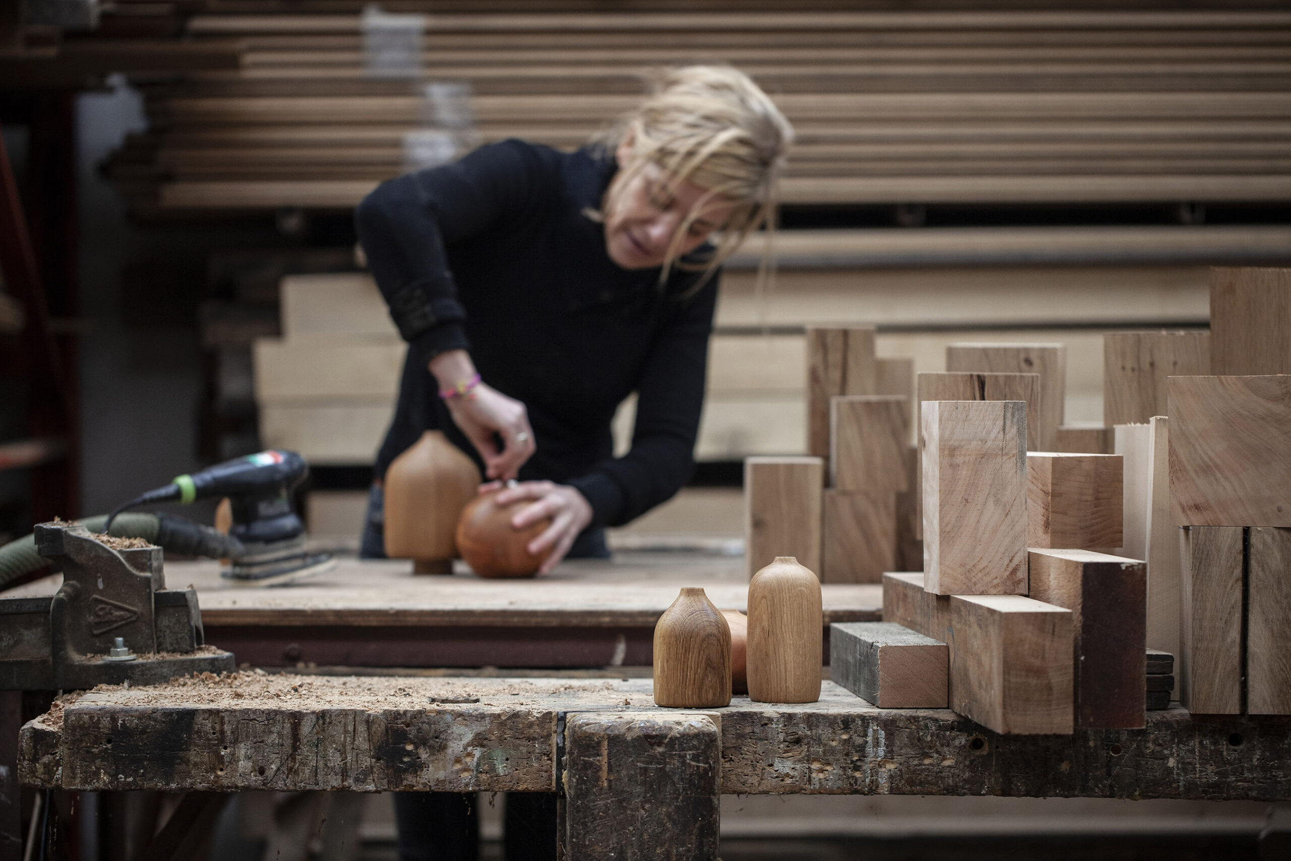 Vue de l'atelier avec les blocs de bois, et Lucille au travail en arrière-plan, tourneuse sur bois dans son atelier à Locre à la frontière belge. Photographie de Nadège Fagoo (Light Motiv)